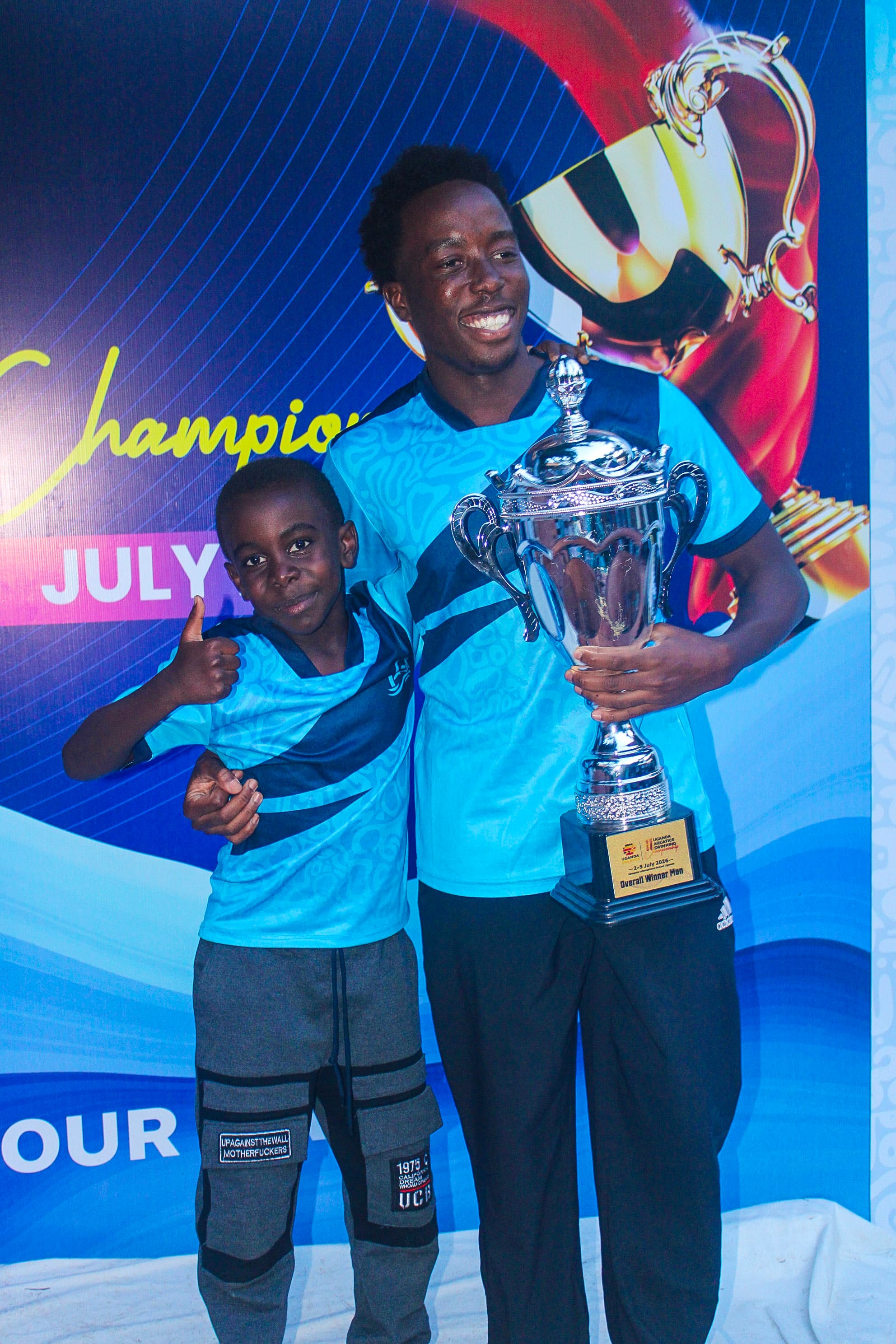 An Imara Aquatics team member and young swimmer holding the national championship trophy